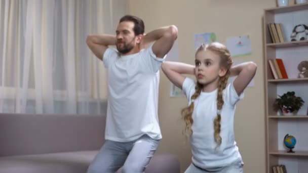 Pai do esporte com a filha fazendo agachamentos em casa, exercícios matinais, disciplina — Vídeo de Stock