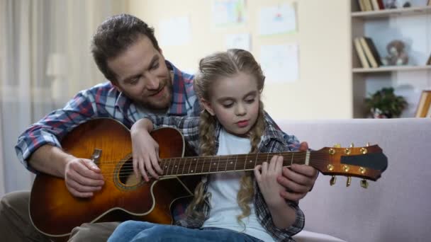 Padre enseñando a su hija a tocar la guitarra en casa, afición musical, ocio familiar — Vídeo de stock