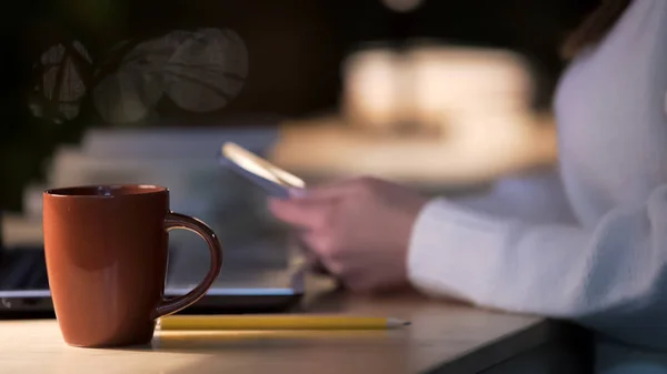 Xícara de café em pé na mesa de café, mulher navegando na internet no celular — Fotografia de Stock