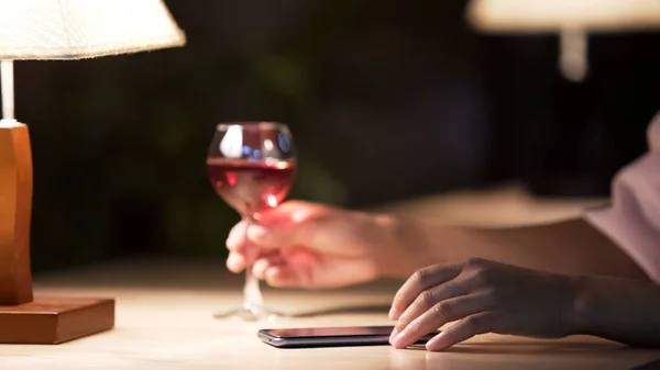 Mujer solitaria desplazándose sitios web en el teléfono celular en la cafetería cómoda, disfrutando del vino —  Fotos de Stock