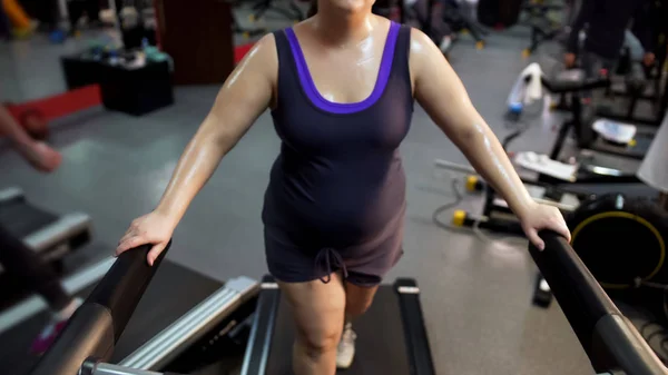 Молодая женщина с большим животом тренируется на беговой дорожке, упорно трудится, чтобы похудеть — стоковое фото