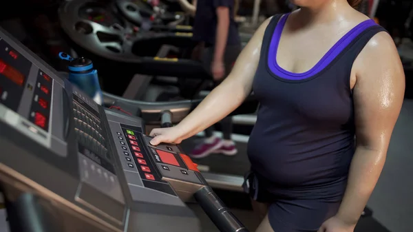 Señora con sobrepeso pulsando botones en el panel de la cinta de correr, comenzando el entrenamiento en el gimnasio —  Fotos de Stock
