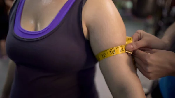 Entrenador que mide los brazos de las mujeres después del entrenamiento en el gimnasio, resultados del programa de pérdida de peso —  Fotos de Stock