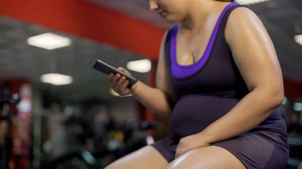 Fat unhealthy woman with big belly checking smartphone app in gym, weightloss — Stock Photo, Image