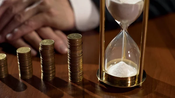 Vidrio de arena y pilas de monedas sobre la mesa, depositante ganando interés en el ahorro — Foto de Stock