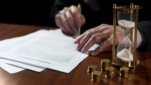 Hombre comprador o vendedor firma acuerdo de compra, dinero y reloj de arena en la mesa — Foto de Stock