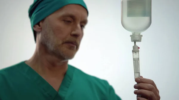 Чоловік-лікар дивиться на падіння ліків в IV обладнання, хіміотерапія — стокове фото