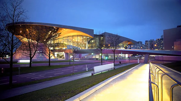 Centre BMW World illuminé à Munich, en soirée, vue depuis la route vide — Photo