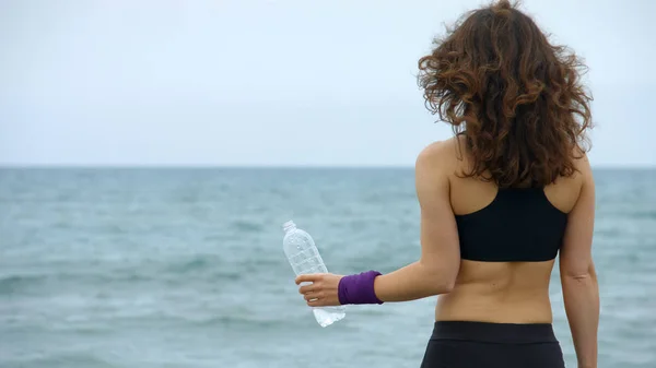 Νεαρή αθλήτρια με μπουκάλι στην παραλία, αίσθημα δίψας μετά από προπόνηση, υγεία — Φωτογραφία Αρχείου