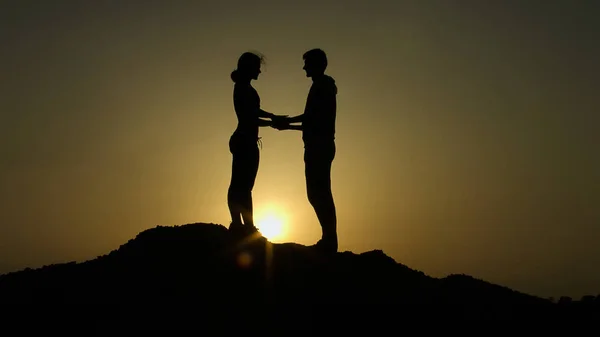 Duas silhuetas seguram as mãos no topo da montanha contra o pôr do sol, superam juntas — Fotografia de Stock