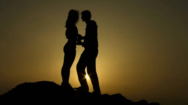 男人抱着女孩的手, 试图亲吻她, 浪漫的时刻在山上日落 — 图库照片