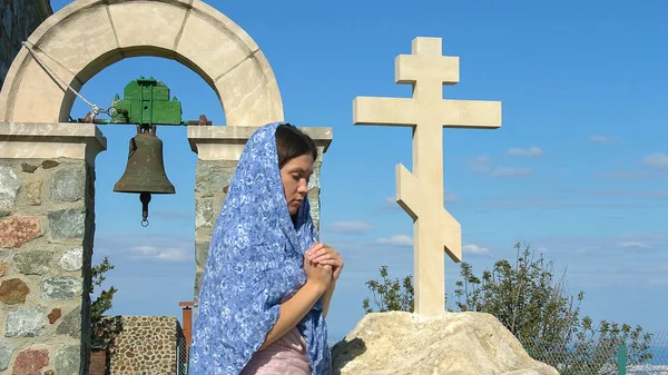 Vreedzame jonge vrouw bidden buiten in de buurt van stone cross, vraagt God voor de zegen — Stockfoto