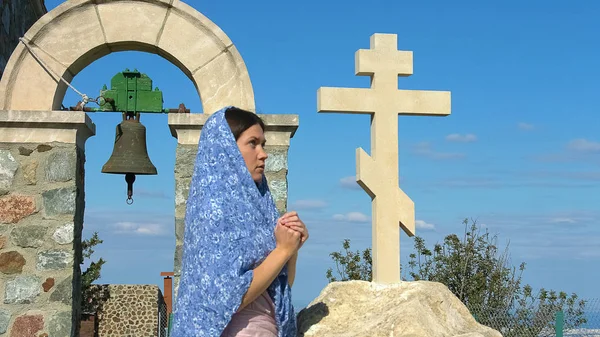 Femme religieuse en foulard priant près de la croix, regardant dans le ciel avec espoir — Photo