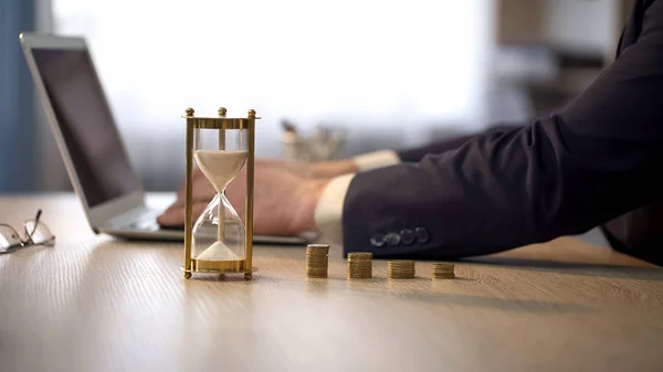 Hombre empleado que trabaja en el ordenador portátil, reloj de arena de pie en el escritorio, la inversión de dinero — Foto de Stock