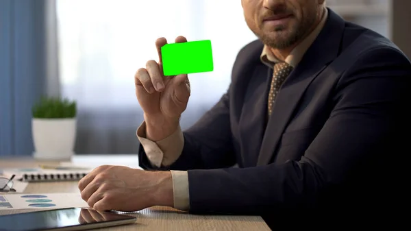 Zaměstnanec sedí v kanceláři, ukazuje kartu v zelené barvě, plán skupinového pojištění — Stock fotografie