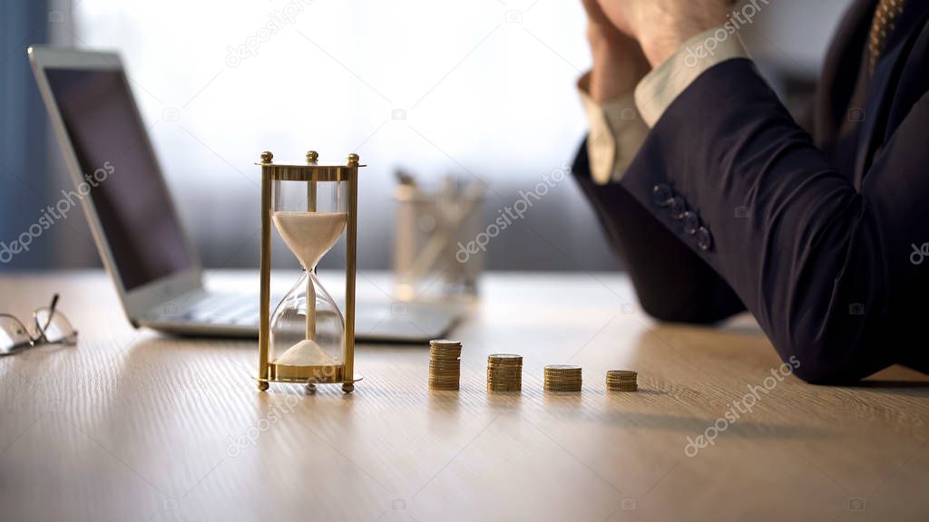 Office worker thinking about income, view of sandglass and stack of coins