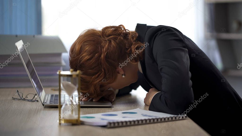 Businesswoman looking at laptop, lying on table, exhaustion, deadline pressure