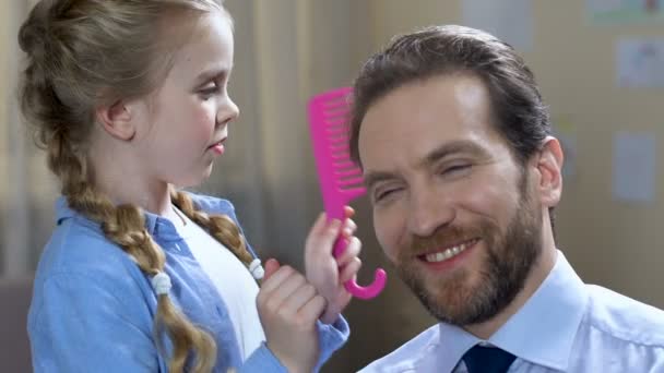 Jogando escola menina pentear o cabelo do pai com escova de cabelo rosa, felizes juntos — Vídeo de Stock