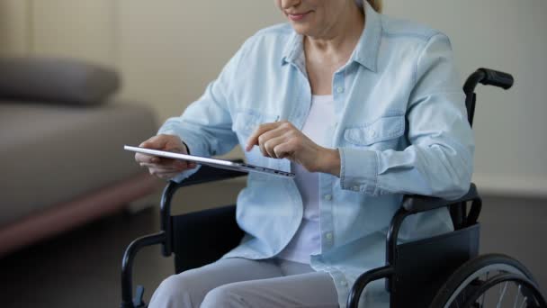 Oma zit in een rolstoel en scrollen familie foto's op tablet, gadget — Stockvideo