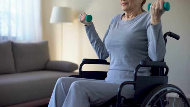 Senior kobieta na wózku inwalidzkim, zniesienie dumbbells, robi ćwiczenia w domu, odzyskiwanie — Wideo stockowe