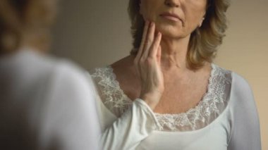 Ayna önünde kırışmış boynuna dokunuyor, süreci yaşlanma Olgun kadın