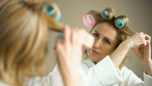 Mujer jubilada arreglando rulos de pelo y preparándose para una cita romántica, apariencia — Vídeo de stock