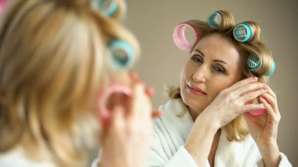 Wanita tua yang cantik menempatkan keriting rambut dan tersenyum ke cermin, trik kecantikan — Stok Video