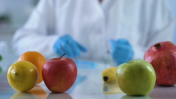 Friss gyümölcsök kutatási táblázat, laboratóriumi munkás fejlődő vitamin lényege, gmo élelmiszerek — Stock videók