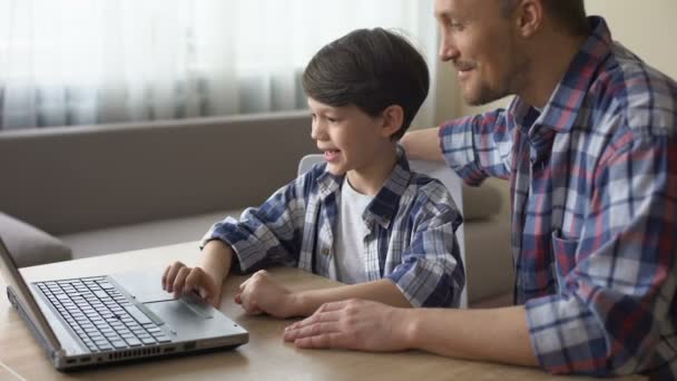 Feliz padre enseñando a su hijo a trabajar en el ordenador portátil en casa, cuidado familiar — Vídeos de Stock