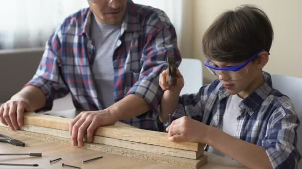 Attentive little boy hammering nail in wooden plank, father supporting his kid — Stock Video