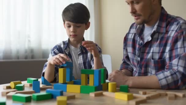 Padre e hijo serio jugando con cubos de juguete, construyendo casa juntos, ocio — Vídeos de Stock