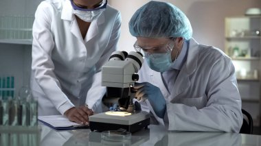 Tıp araştırmacısı mikroskop ve meslektaşım not almak, laboratuvar arıyor