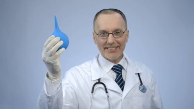 Funny doctor holding rectal syringe with smile on face, proctologist joking clipart