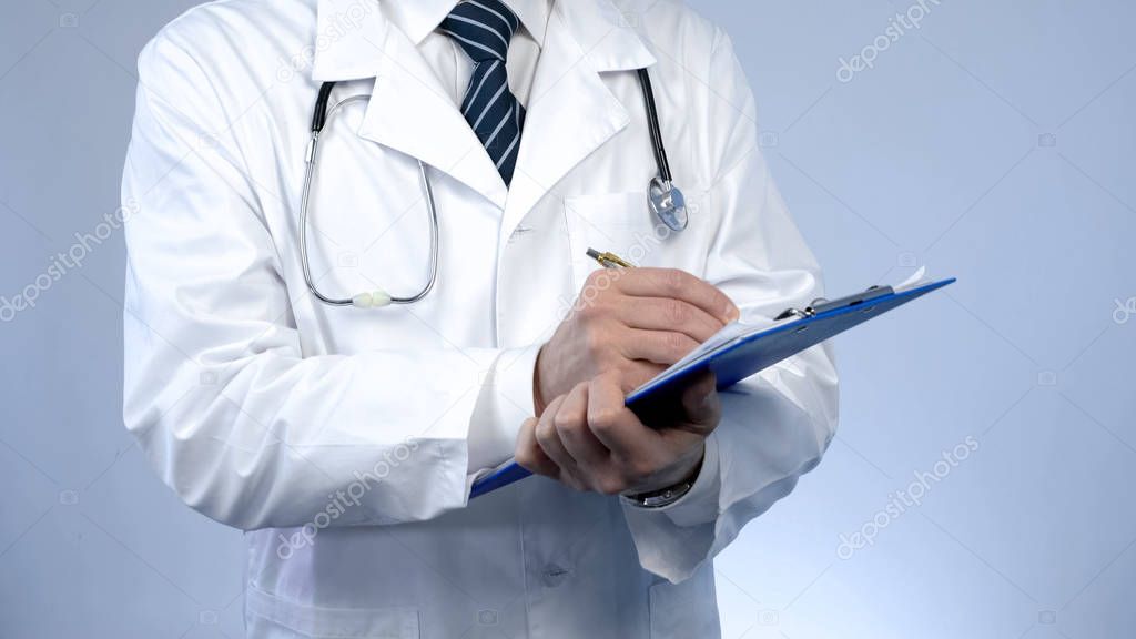 Professional physician writing in paper documents, keeping medical records