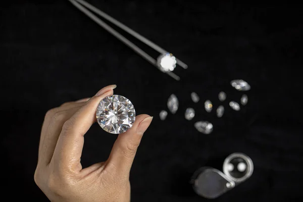 The jeweller holds large diamond in hand on black background. Close-up polished round diamond.