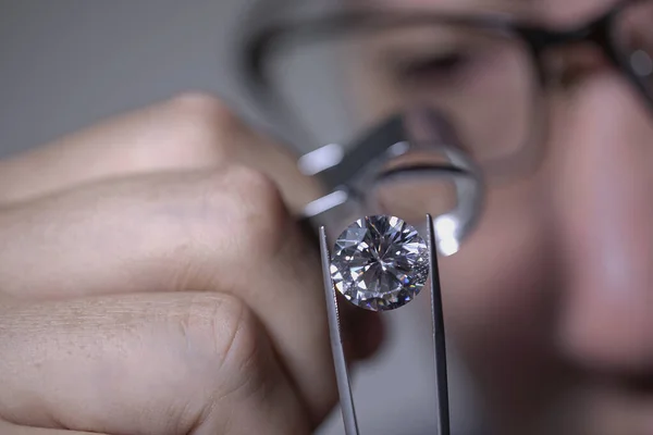 Man jeweller looking through loupe to diamond. Cut and polished diamond. Diamond grading. Diamond trading. Diamond sales. Jeweller holding magnifier. Round diamond. Jeweller on black background