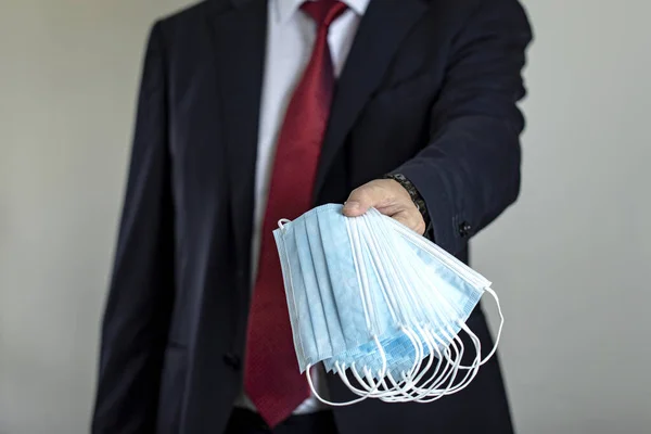 Businessman in suit with red tie is holding medical masks. Medical mask. Surgery masks. Busines stop coronavirus. COVID-19. Pandemia, industry. Director giving medical masks.