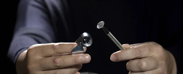 Man jeweller holding round shape diamond. Jewellery business. Diamond industry. Cut and polished diamonds. Loupe, magnifier. Diamond tools. Loose diamond. Luxary gem stones. Precious stones. Diamond sales, grding, trading.