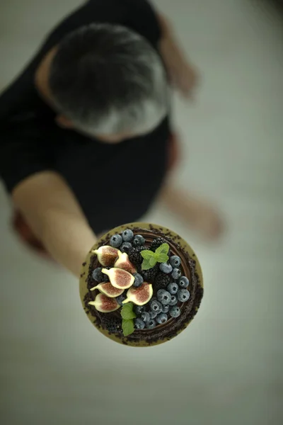 Grey haired man holding plate with blueberries, blackberries, figs and mint. Fruits and berries. Healthy food. Vegan food. Blue berry, Black berry, fig, mint. Top up view.