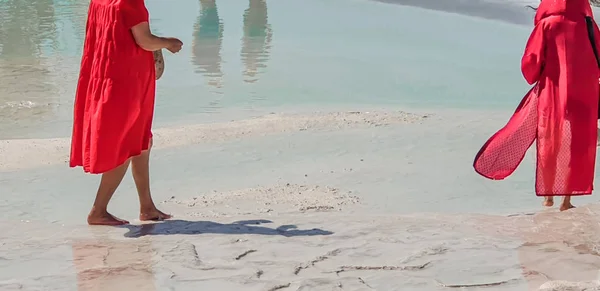 Pamukkale, Türkiye 'de beyaz travertinlerde uzun kırmızı elbiseli genç çıplak ayaklı kızlar.
