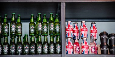 Heineken bira şişeleri ile birlikte Firefly içecek şişeleri ve günlük bardaklar bir rafta dizilmiş..