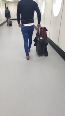 Trol çantasıyla Amsterdam 'daki Schipol havaalanındaki uçağa doğru yürüyen bir yolcu.
