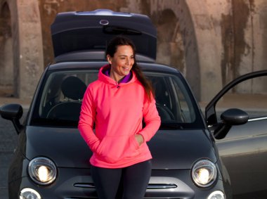 Fuşya formalı kadın, gün batımında arabanın yanında.