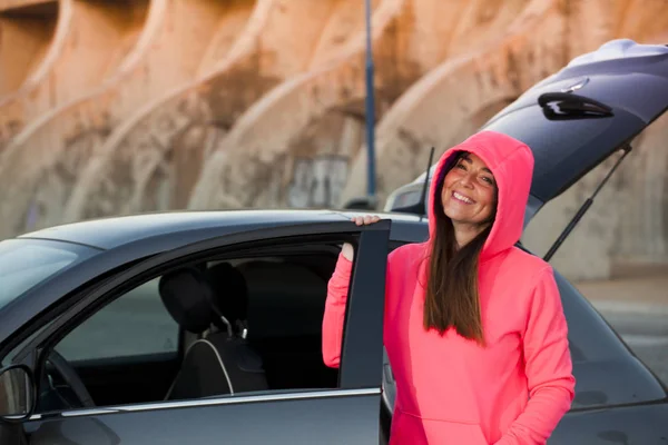 woman with fuchsia sweater, next to the gray car