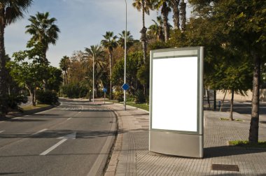 Şehir merkezindeki yol üzerinde palmiye ağaçları olan ilan panosu.
