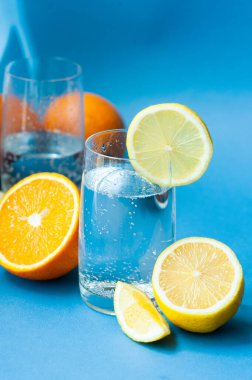 köpüklü, limonlu, limonlu, limonlu, limonlu ve portakallı iki bardak berrak su mavi arka planda. C vitamini al, bağışıklığı güçlendir