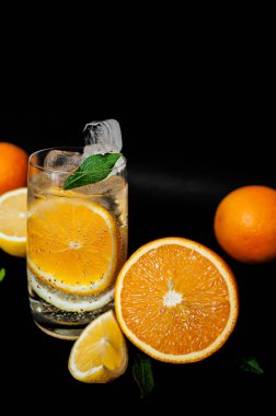 İçi kabarcıklı su dolu şeffaf cam, içi turuncu yuvarlak dilim, buz ve nane yaprağı, stüdyo ışıklarında siyah arka planda yarı sulu ve olgun portakal ve limon. Menüler ve içerik için fotoğraflar