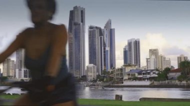 Surfers paradise, Australia - February 29, 2020: Boats travel along the Nerang River and female riding bike with Surfers paradise high rise buildings backdrop
