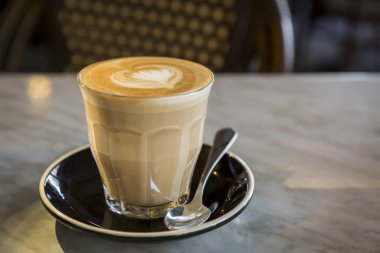 Kahve fincanındaki kahve, aşk dolu kalp şeklinde sütlü latte, mermer masa ve kahve dükkanındaki retro sandalye.