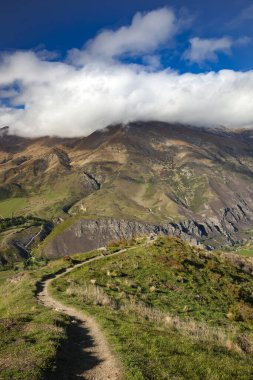 Yeni Zelanda dağ yolu otlar ve tarlalar arasında, dağ tepesi bulutları, dikey fotoğraf, Yeni Zelanda.